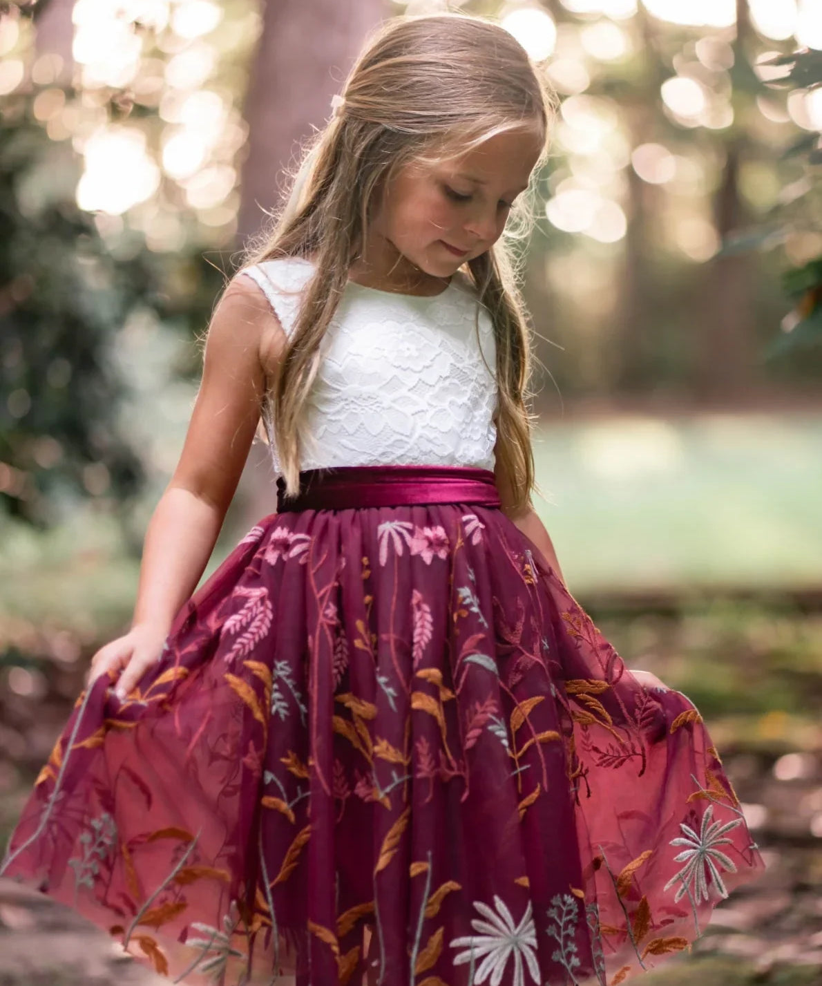 Girl wearing burgundy embroidered flower girl dress with white lace bodice