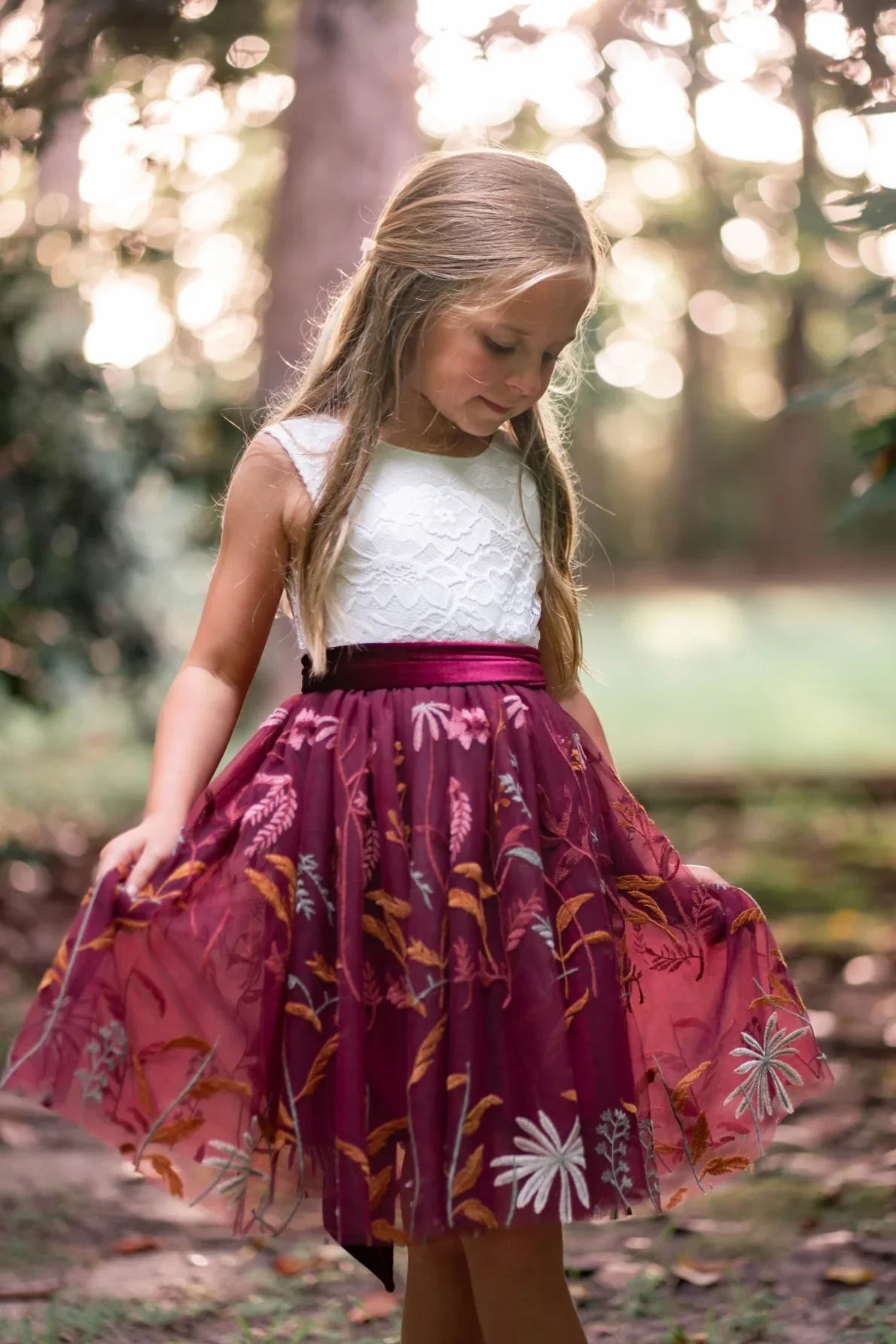 Girl wearing burgundy embroidered flower girl dress with white lace bodice