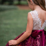 Toddler girl in burgundy flower girl dress walking outdoors