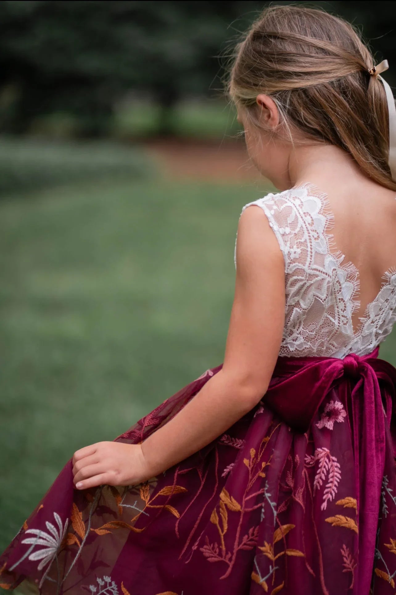 Toddler girl in burgundy flower girl dress walking outdoors