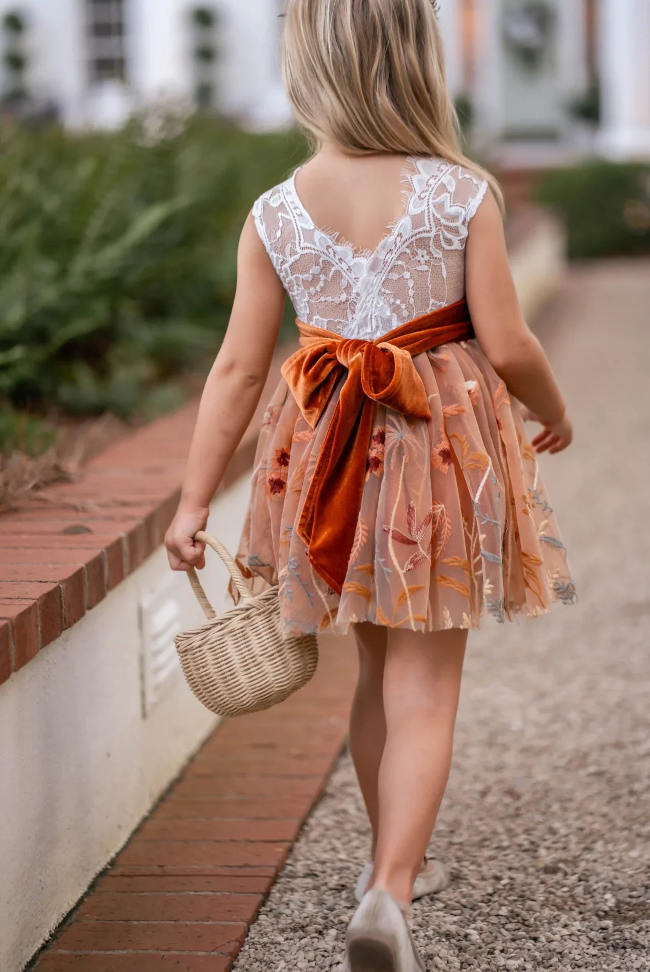 Back view of white lace and burnt orange embroidered fall flower girl dress tied with a velvet sash