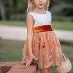 Front view of girl wearing burnt orange floral embroidered flower girl dress with white lace bodice and velvet sash