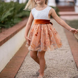 Girl twirling in white lace and burnt orange floral embroidered knee-length dress
