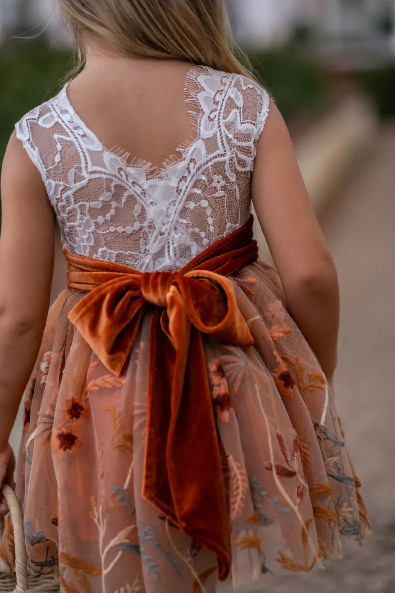 Girl walking in rustic outdoor setting wearing lace and burnt orange fall flower girl dress