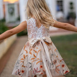 Back view of girl in sleeveless white lace and champagne flower girl dress walking outdoors
