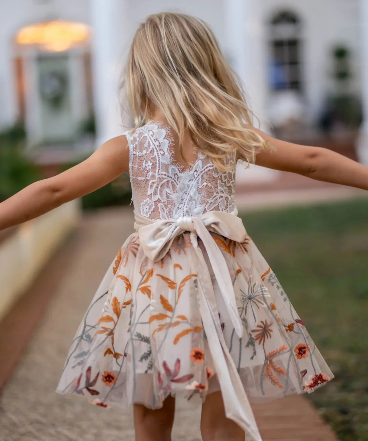 Back view of girl in sleeveless white lace and champagne flower girl dress walking outdoors