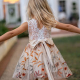 Back view of girl in sleeveless white lace and champagne flower girl dress walking outdoors