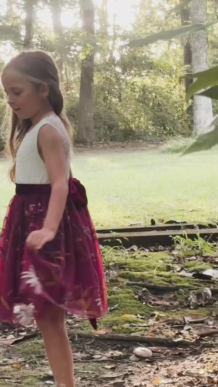 Video of girl twirling in burgundy floral embroidered flower girl dress with white lace bodice and velvet sash”

